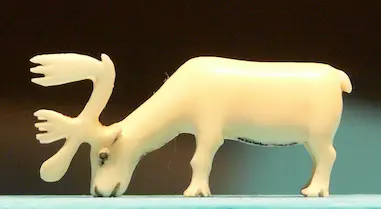 A small white ivory carving of a caribou with its head down, grazing