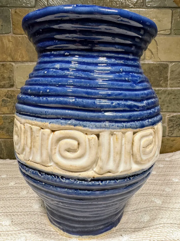 A blue glazed student pot with visible coils and a white spiral band
