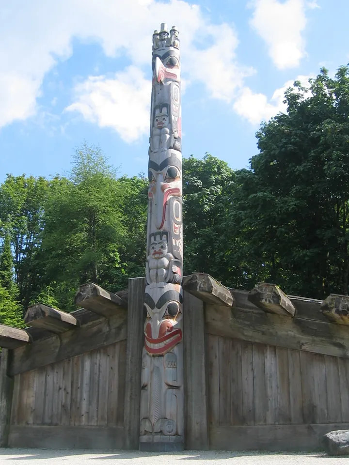 A tall carved pole in front of a cedar plank house