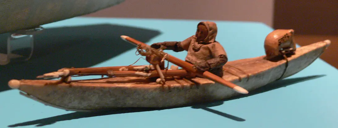 A model kayak with a carved paddler holding a long paddle