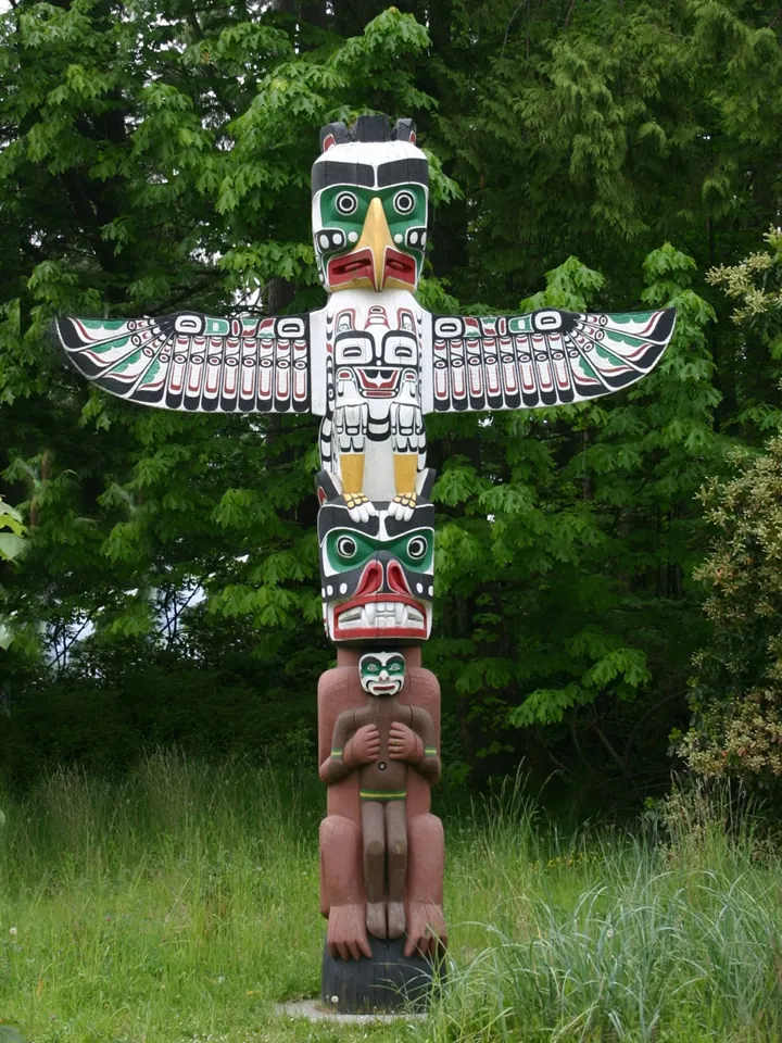 A tall carved and painted pole topped by a thunderbird with outstretched wings