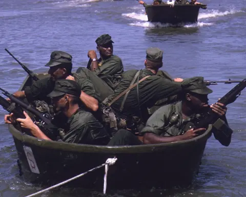 American soldiers paddling a small round boat through dense vegetation during the Vietnam War